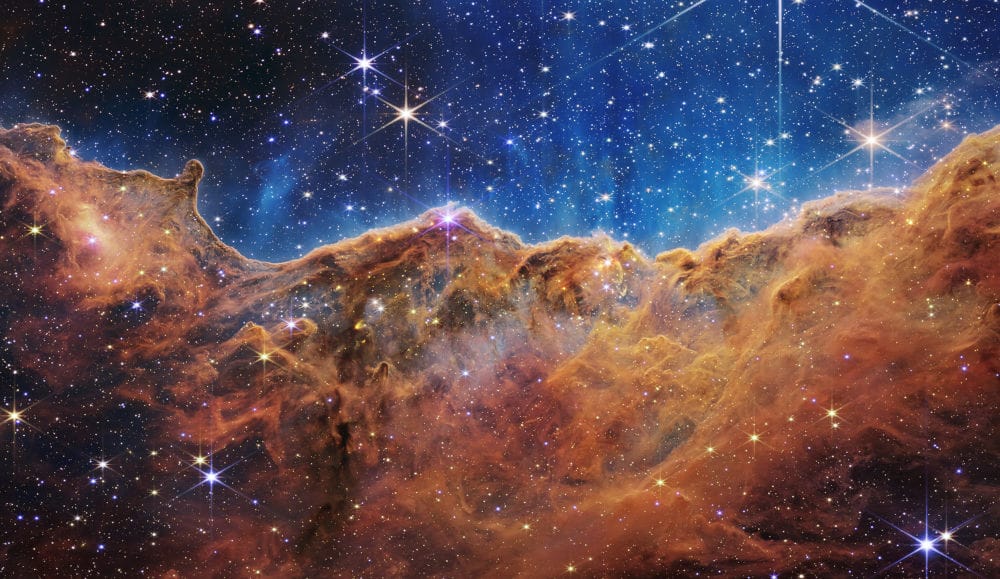 غيوم برتقالية في أسفل الصورة هي الجروف الكونية و في أعلى الصورة تظهر خلفية الفضاء زرقاء مع بعض السواد مع نقط بيضاء صغيرة هي نجوم بعيدة