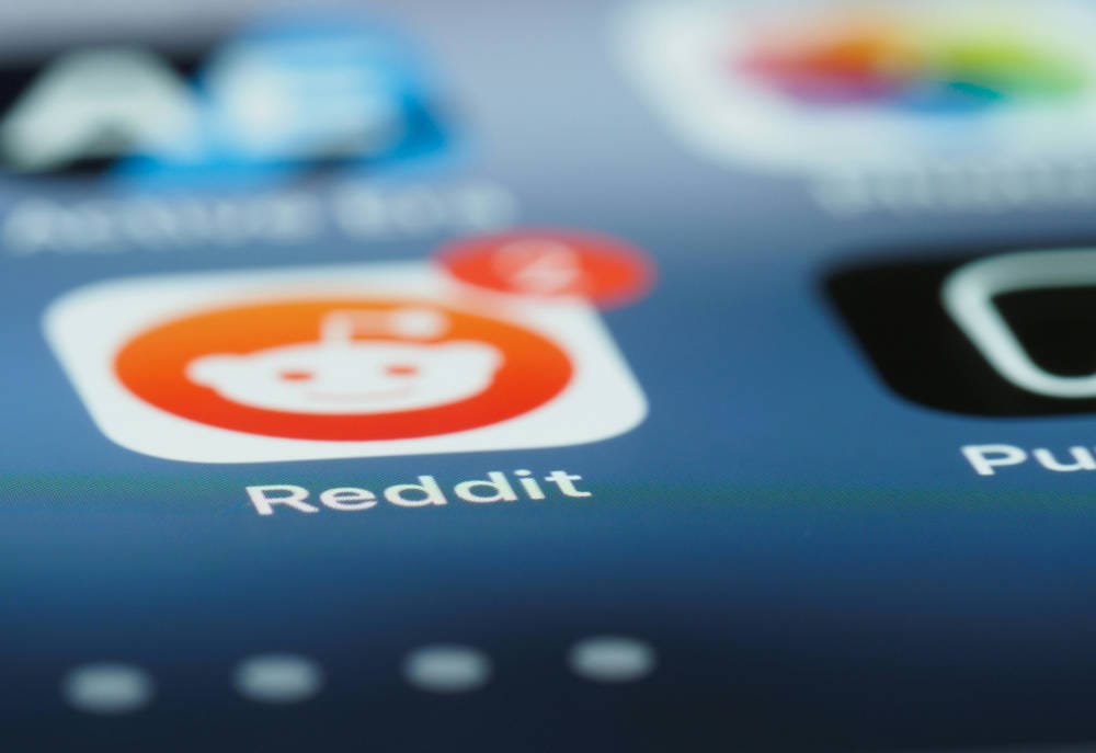 أيقونة تطبيق ريديت الذي فيه وجه أبيض ورائه دائرة لونها برتقالي و حول الدائرة إطار مربع لونه أبيض، ويظهر في الزاوية العلوية للأيقونة دائرة برتقالية فيها الرقم 2. الصورة لمقالة عن اتفاق بين جوجل و ريديت.